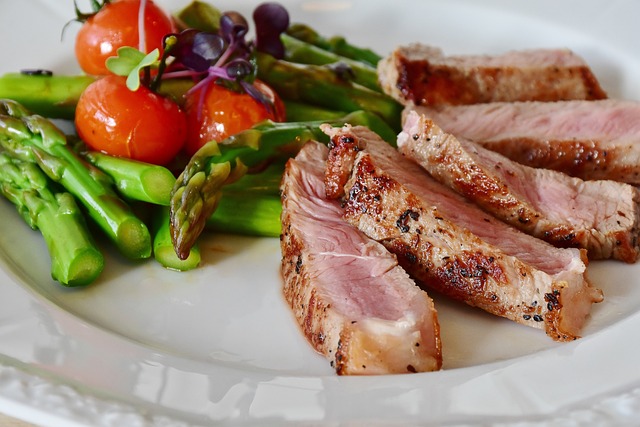 Ein weißer Teller mit angebratenen Steakscheiben, einer Beilage gegrilltem Spargel und Kirschtomaten, garniert mit Microgreens. Das Steak wirkt saftig und innen leicht rosa, perfekt für die beste Ernährung eines Fußballers. Das Gemüse sieht frisch und lebendig aus.