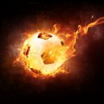 Ein von hellen, feurigen Flammen umhüllter Fußball scheint vor einem dunklen Hintergrund durch die Luft zu fliegen und veranschaulicht dynamische Energie und Bewegung.