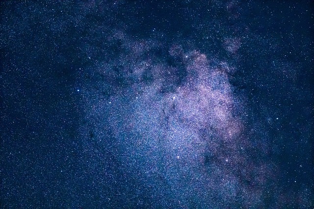 Ein dichter, sternenübersäter Nachthimmel mit einer markanten, wolkenähnlichen Formation in der Mitte zeigt die Milchstraße vor einem tiefdunklen, blauen Hintergrund. Die Sterne variieren in ihrer Helligkeit und erzeugen eine mystische und ehrfurchtgebietende Himmelsszene, die an die Erkundung des riesigen Universums durch Astrokartografie erinnert.