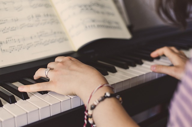 Eine Person spielt Klavier und hat Notenblätter vor sich. Sie trägt Ringe an den Fingern und ein Armband. Der Fokus liegt auf den Händen und den Klaviertasten, was vielleicht ihr Engagement für das Klavierlernen über Online-Unterricht hervorhebt.