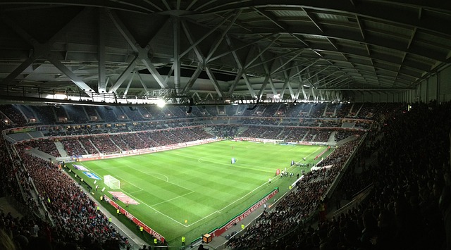 Panoramablick auf ein hell erleuchtetes, voll besetztes Fußballstadion bei Nacht. Das Feld ist grün und bereit zum Spiel, die Fans füllen voller Vorfreude die Tribünen. Die tragenden Balken des Stadions sind sichtbar und tragen zur großartigen Atmosphäre bei – ein wahrer Schlüssel zum Erfolg für Sportwetten-Profis.